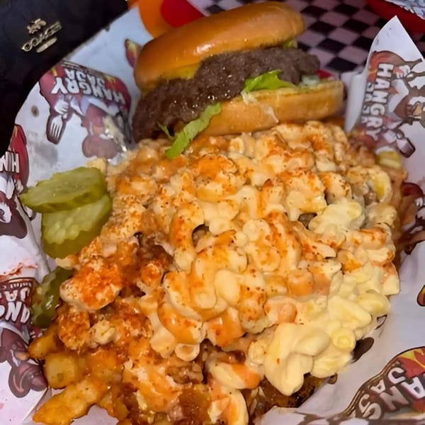 A Hangry JAJA burger with lettuce and a side of fries topped with mac and cheese and pickles.