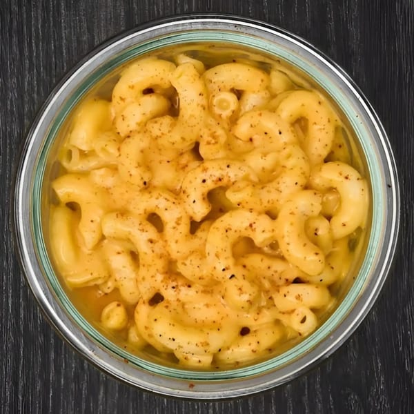 Top-down view of Hangry JAJA's mac and cheese, seasoned with pepper, in a clear glass bowl.