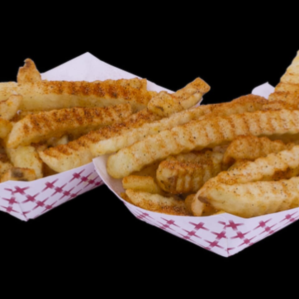 Two paper trays filled with seasoned crinkle-cut fries against a black background.