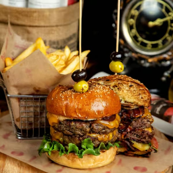 Two large, stacked burgers with cheese, lettuce, and olives, next to a basket of fries.